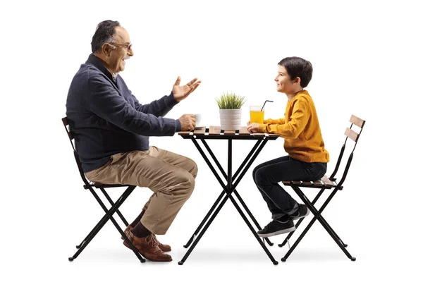 祖父はカフェのテーブルに座って白い背景に隔離された孫と話しています — ストック写真