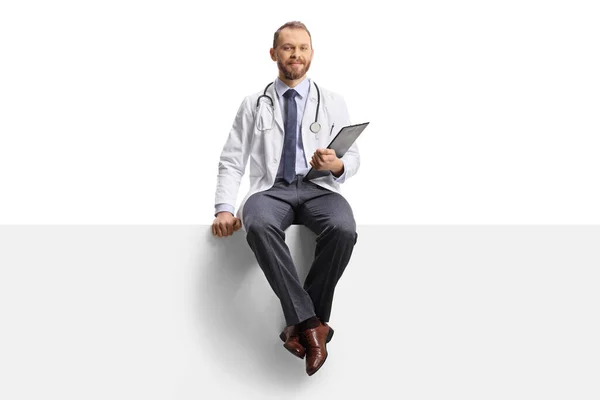 Médico Masculino Sonriendo Sentado Panel Blanco Con Portapapeles Las Manos — Foto de Stock