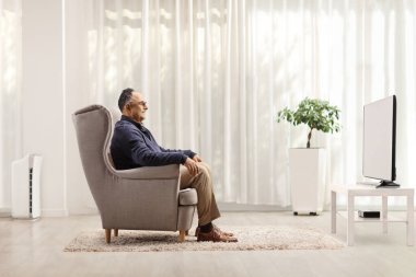 Olgun bir adamın oturduğu koltukta oturup evde televizyon izlediği profil fotoğrafı.