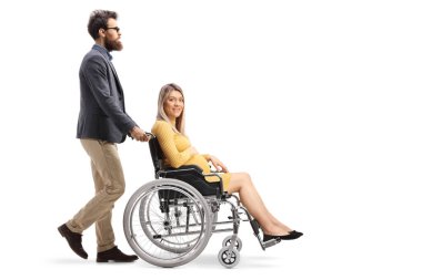 Sakallı bir adamın, beyaz arka planda izole edilmiş tekerlekli sandalyedeki hamile bir kadını iterken tam boy profil fotoğrafı.