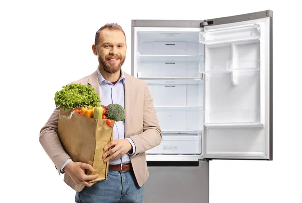 Молодий Випадковий Чоловік Тримає Продуктовий Мішок Перед Відкритим Порожнім Холодильником — стокове фото