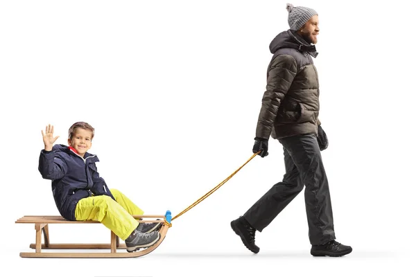 一个身穿冬衣的父亲在白色背景的雪橇上走着拉着一个男孩的全景照片 — 图库照片