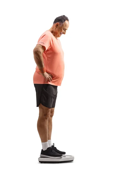 白い背景に隔離された体重計の上に立つスポーツウェアの成熟した男の完全な長さのプロフィールショット — ストック写真