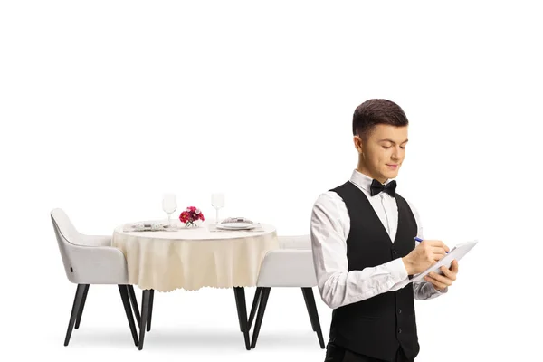 白い背景に隔離されたレストランテーブルの前に蝶ネクタイを持つウェイター — ストック写真
