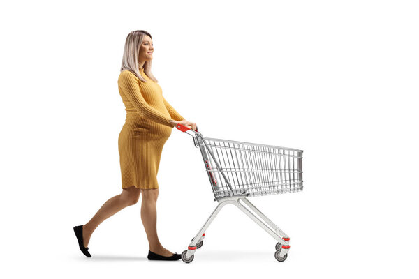 Full length profile shot of a pregnant woman pushing an empty shopping cart isolated on white background