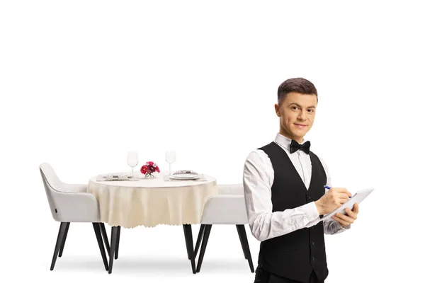白い背景に隔離されたレストランテーブルの前に弓タイを持つ若い男性ウェイター — ストック写真