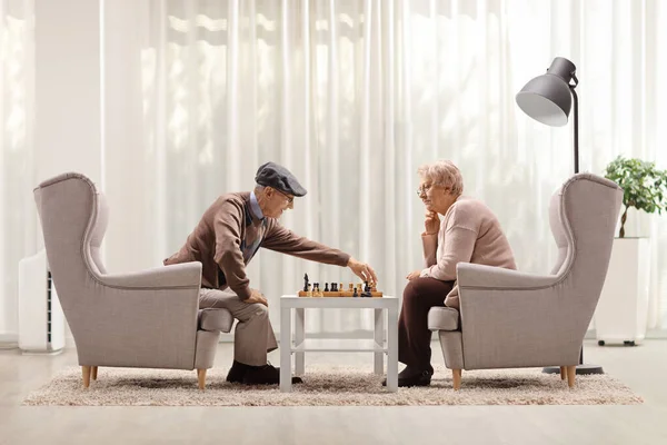 老人と女性座っていますアームチェアに自宅でとチェスをプレイ — ストック写真
