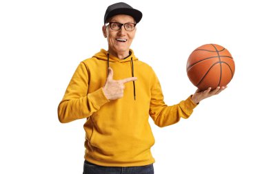 Sarı eşofmanlı neşeli yaşlı bir adam elinde basketbol topuyla beyaz arka planı işaret ediyor.