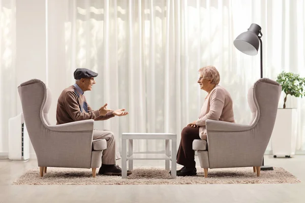 高齢者の男性と女性がアームチェアに座って リビングルームで自宅で会話をしています — ストック写真