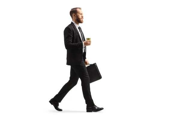 テイクアウトコーヒーカップと白い背景に隔離されたブリーフケースで歩くビジネスマンの完全な長さのプロフィールショット — ストック写真