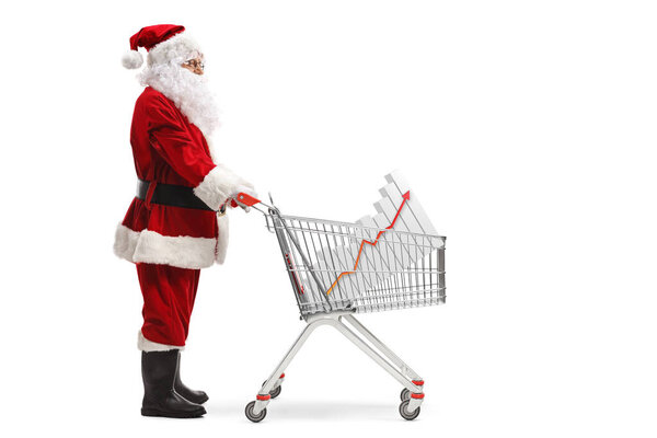 Full length profile shot of Santa Claus standing with a shopping cart and a bar chart inside isolated on white background