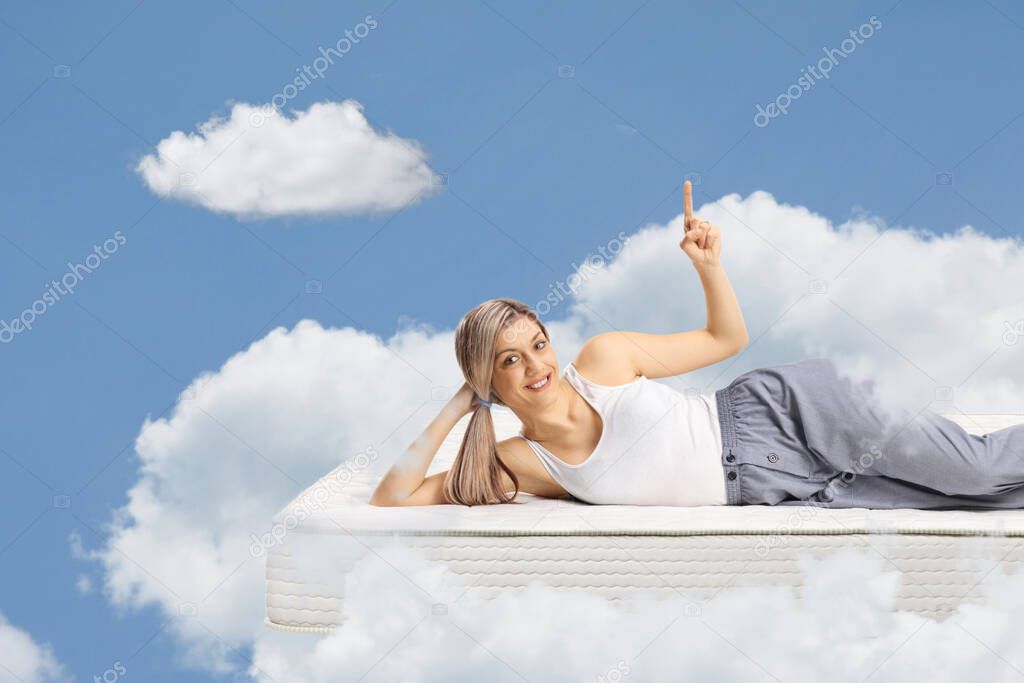Young woman lying on a mattress in pajamas and pointing up to the sky