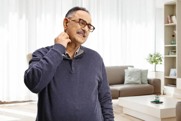 Mature man itching his neck at home in a living room