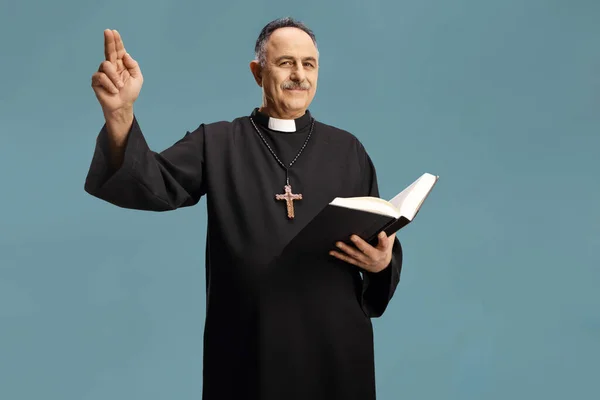 成熟的牧师从圣经中读出一篇祷文 用蓝色背景隔离的手给自己做手势 — 图库照片