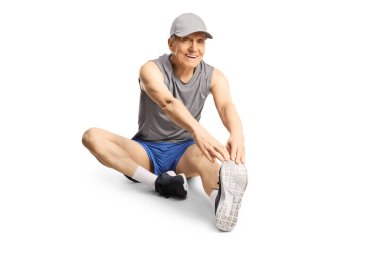Spor kıyafetli yaşlı bir adam bacağını uzatıyor ve beyaz arka planda izole bir şekilde yerde oturuyor.