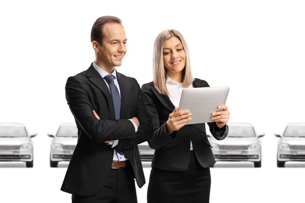 Woman showing a tablet to a businessman in front of new silver cars isolated on white background