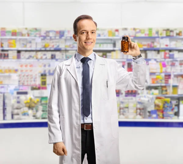 Mężczyzna Farmaceuta Pokazując Butelkę Pigułek Patrząc Aparat Fotograficzny Wewnątrz Apteka — Zdjęcie stockowe