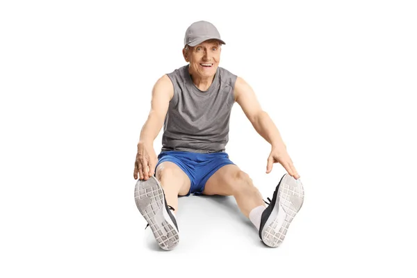 スポーツウェアを着た高齢者が床に足を伸ばし 白い背景に隔離された笑顔 — ストック写真