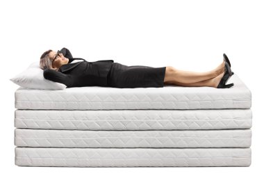 Beyaz arka planda izole edilmiş bir şilte yığınının üzerinde yatan iş kadını