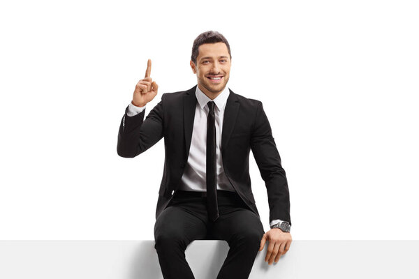Businessman sitting on a blank panel and pointing up isolated on white background