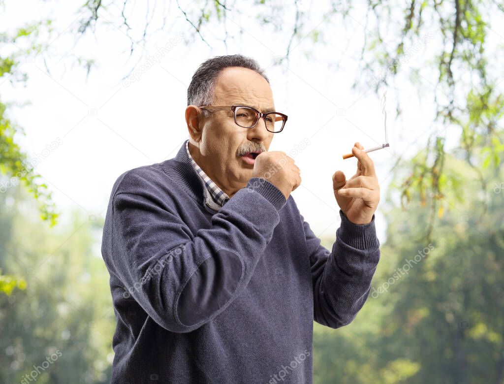 Mature man smoking and coughing outdoors in a park