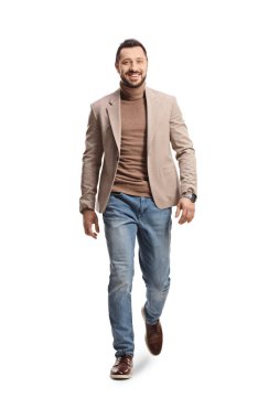 Beyaz arka planda izole edilmiş kameraya doğru yürüyen bej takım elbiseli ve kot pantolonlu bir gencin tam boy portresi.