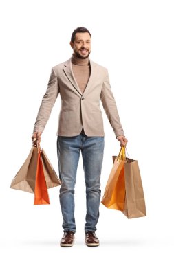 Beyaz arka planda izole edilmiş alışveriş torbaları tutan bej takım elbiseli ve kot pantolonlu zarif bir adamın tam boy portresi.