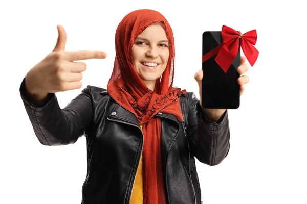 Mladá Žena Hidžábem Drží Smartphone Červenou Mašlí Ukazuje Izolované Bílém — Stock fotografie