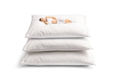 Beyaz arka planda büyük yastıkların üzerinde uyuyan pijamalı hamile bir kadın.