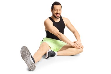 Spor kıyafetli genç adam beyaz arka planda izole bir şekilde bacağını esnetiyor.