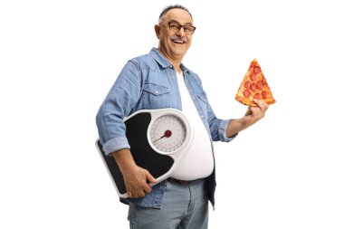 Bir dilim biberli pizzayla neşeli olgun bir adam beyaz arka planda izole edilmiş ağırlık tartısını tutuyor.