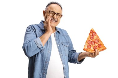 Diş ağrısı olan olgun bir adam beyaz arka planda izole edilmiş bir dilim pepperoni pizza tutuyor.