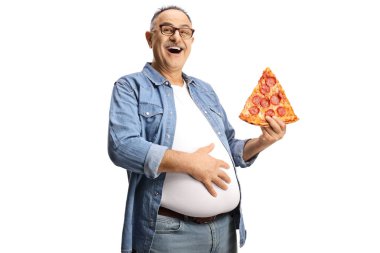 Bir dilim biberli pizzayla neşeli olgun bir adam karnını tutuyor ve beyaz arka planda izole bir şekilde gülümsüyor.