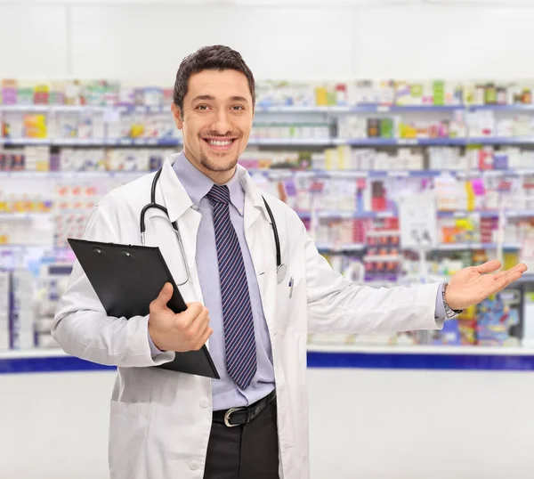 Cheerful Young Doctor Holding Clipboard Gesturing Welcome Phamracy — стоковое фото