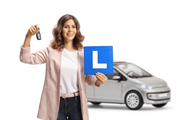 年轻女子在一辆白色背景的银色轿车前拿着汽车钥匙和学习盘 — 图库照片
