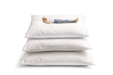 Beyaz arka planda izole edilmiş büyük yastıkların üzerinde pijamalı genç bir kadın yatıyor.