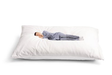 Beyaz arka planda büyük yumuşak bir yastıkta uyuyan pijamalı adam.