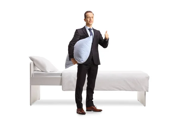 商人拿着枕头 把大拇指伸向床旁边 床与白色背景隔离 — 图库照片