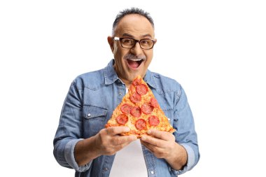 Neşeli olgun bir adam pepperonili pizza yiyor ve beyaz arka planda izole edilmiş kameraya bakıyor.