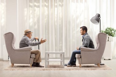 Büyükbabam ve torunum koltuklarda oturmuş evde sohbet ediyorlar.