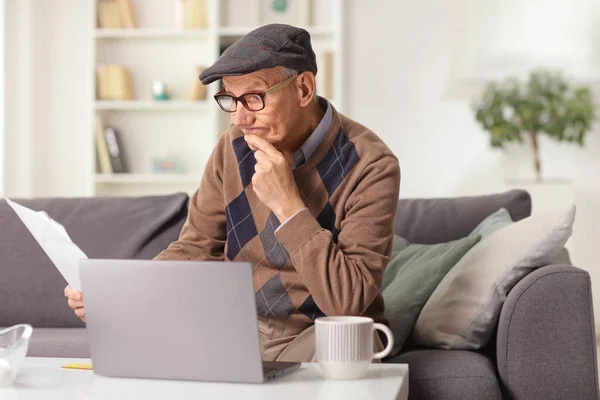 Elderly Man Sitting Sofa Home Reading Paper Document Laptop Computer — Zdjęcie stockowe