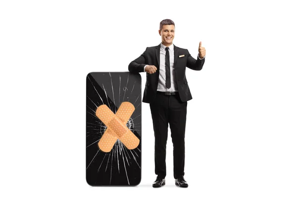 Man Black Suit Leaning Smartphone Broken Screen Bandage Gesturing Thumbs — Stok fotoğraf