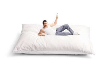 Pijamalı genç adam büyük bir yastığın üzerinde uzanıyor ve beyaz arka planda izole edilmiş bir şekilde duruyor.