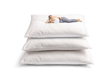 Beyaz arka planda izole edilmiş pijamalarıyla yastık yığınının üzerinde yatan genç bir kadın.