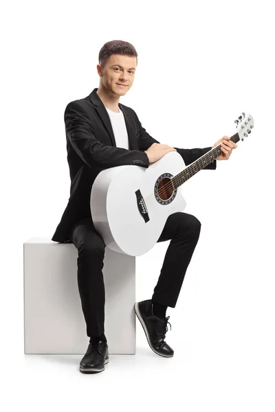 Ung Man Svart Kostym Med Akustisk Gitarr Sitter Vit Kub — Stockfoto