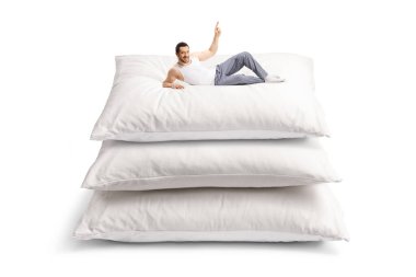 Genç adam pijamalı bir yastık yığınının üzerinde yatıyor ve yukarıdaki izole edilmiş beyaz arka planı işaret ediyor.