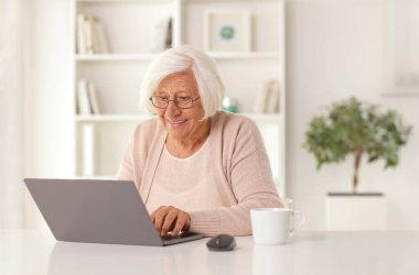 Evde dizüstü bilgisayar kullanan yaşlı bir kadın.