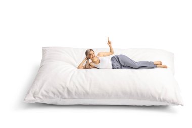 Pijamalı, rahat bir yastığın üzerinde uzanmış gülümseyen genç kadın ve beyaz arka planda izole bir şekilde duran.