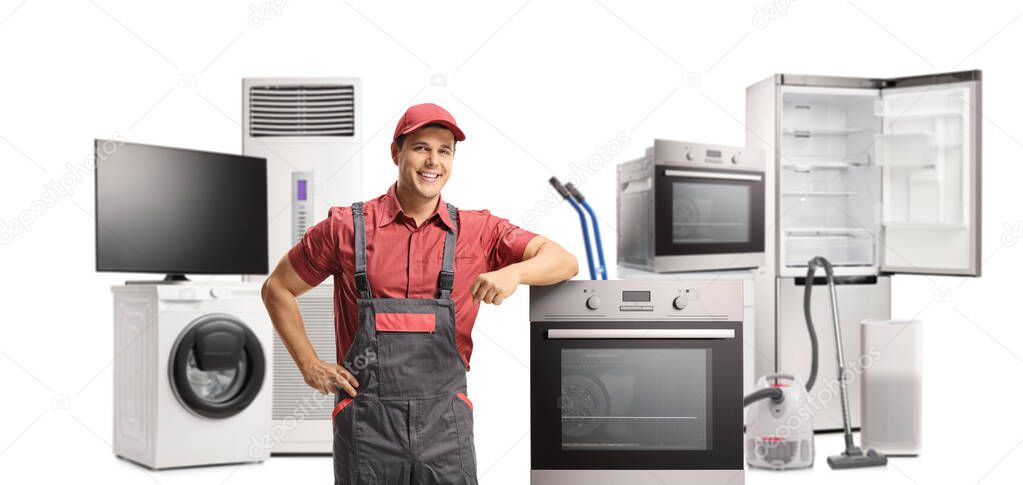 Repairman in a uniform standing next to an electric oven and other appliances isolated on white background