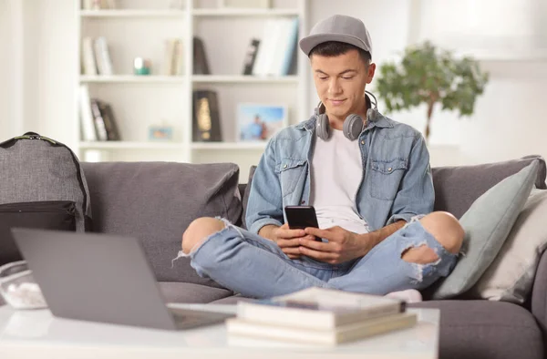 Młody Człowiek Telefonami Komórkowymi Piszący Smartfonie Siedzący Kanapie Domu — Zdjęcie stockowe